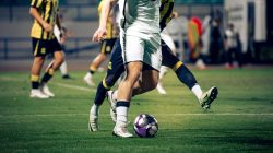 Gambar close-up para pemain sepak bola yang sedang beraksi selama pertandingan di stadion terbuka.