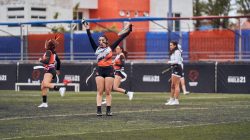 Para pemain wanita merayakan setelah mencetak gol dalam pertandingan flag football di lapangan terbuka yang semarak.