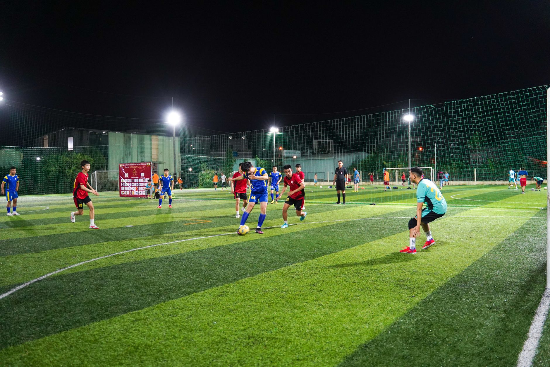 Atlet muda bermain pertandingan sepak bola kompetitif di lapangan rumput buatan yang diterangi di malam hari.