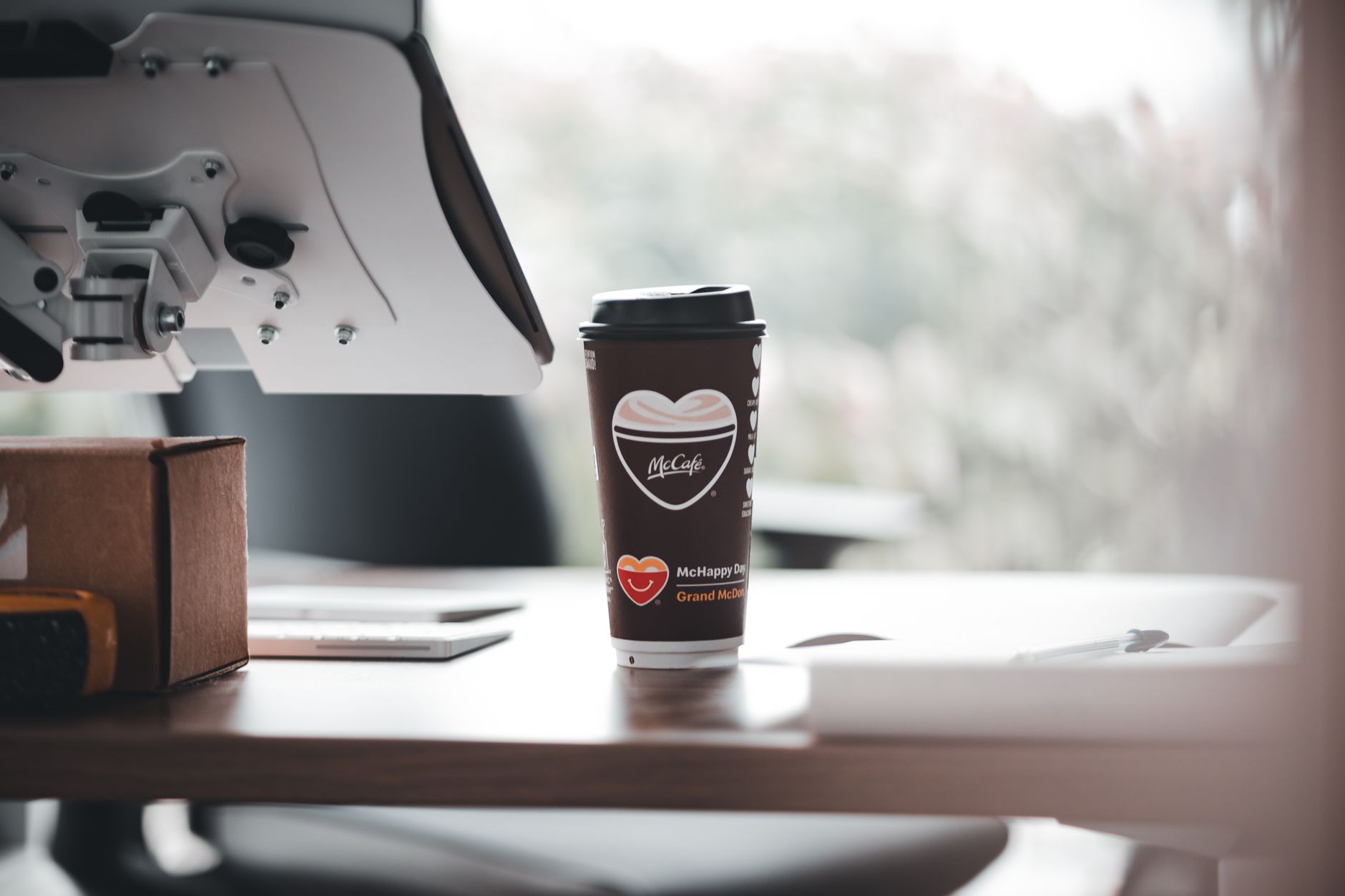 Cangkir kopi bermerek McCafe di meja kantor modern, menciptakan suasana kerja yang santai.