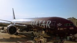 Pesawat Qatar Airways dengan branding Piala Dunia FIFA 2026 di terminal bandara di bawah langit jernih.