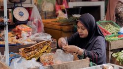 Adegan pasar Indonesia dengan seorang penjual wanita yang mengatur hasil bumi. Suasana pasar yang hidup dan otentik.