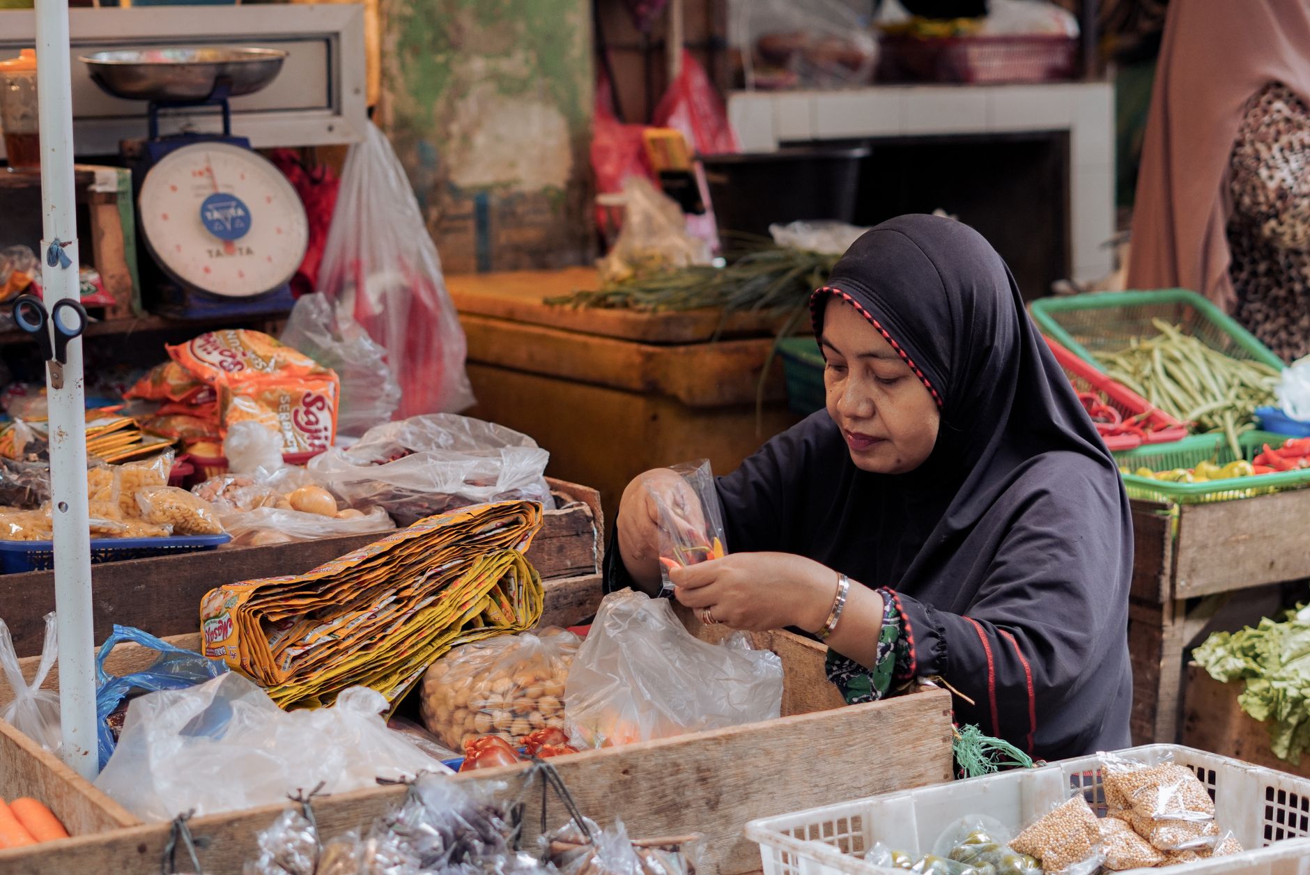 Adegan pasar Indonesia dengan seorang penjual wanita yang mengatur hasil bumi. Suasana pasar yang hidup dan otentik.