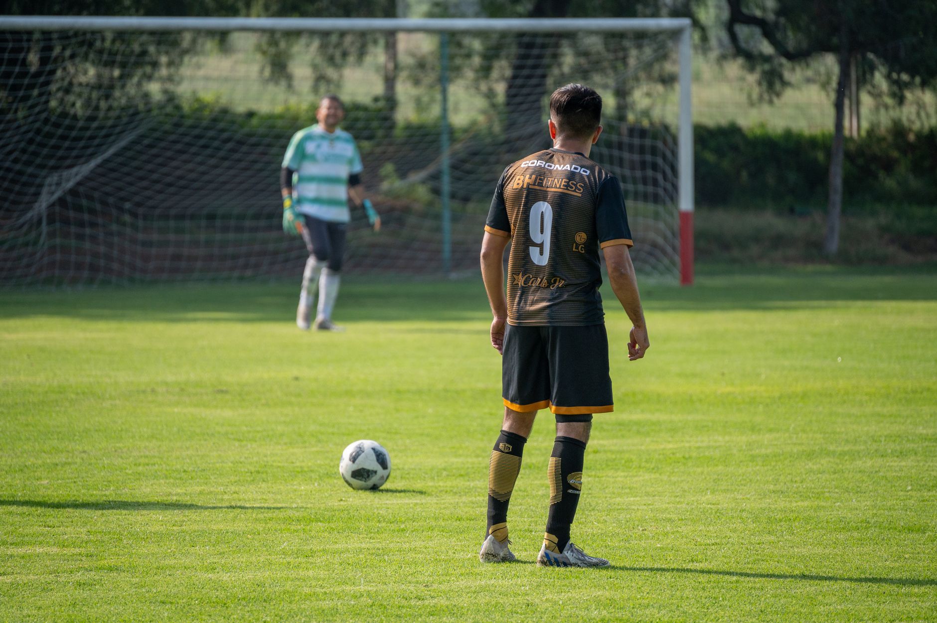 Pemain sepak bola dalam aksi bersiap untuk tendangan penalti di hari yang cerah di lapangan hijau.