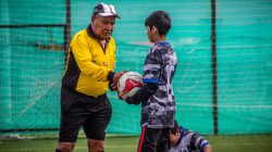 Seorang pelatih dewasa dan pemain muda selama sesi latihan sepak bola di luar ruangan di Chili.