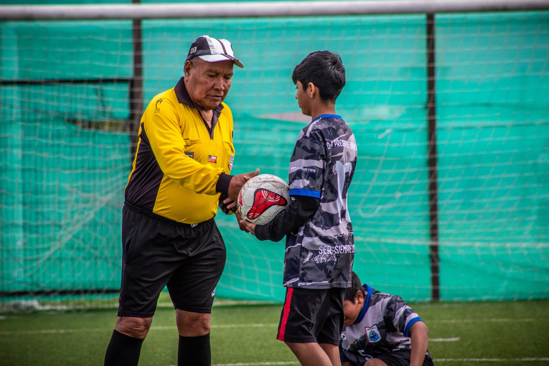 Seorang pelatih dewasa dan pemain muda selama sesi latihan sepak bola di luar ruangan di Chili.
