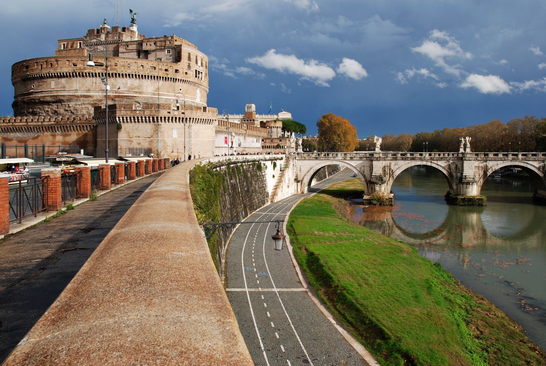 Castel Sant'Angelo bersejarah di Roma yang menghadap ke Sungai Tiber dan jembatan di bawah langit yang dramatis.