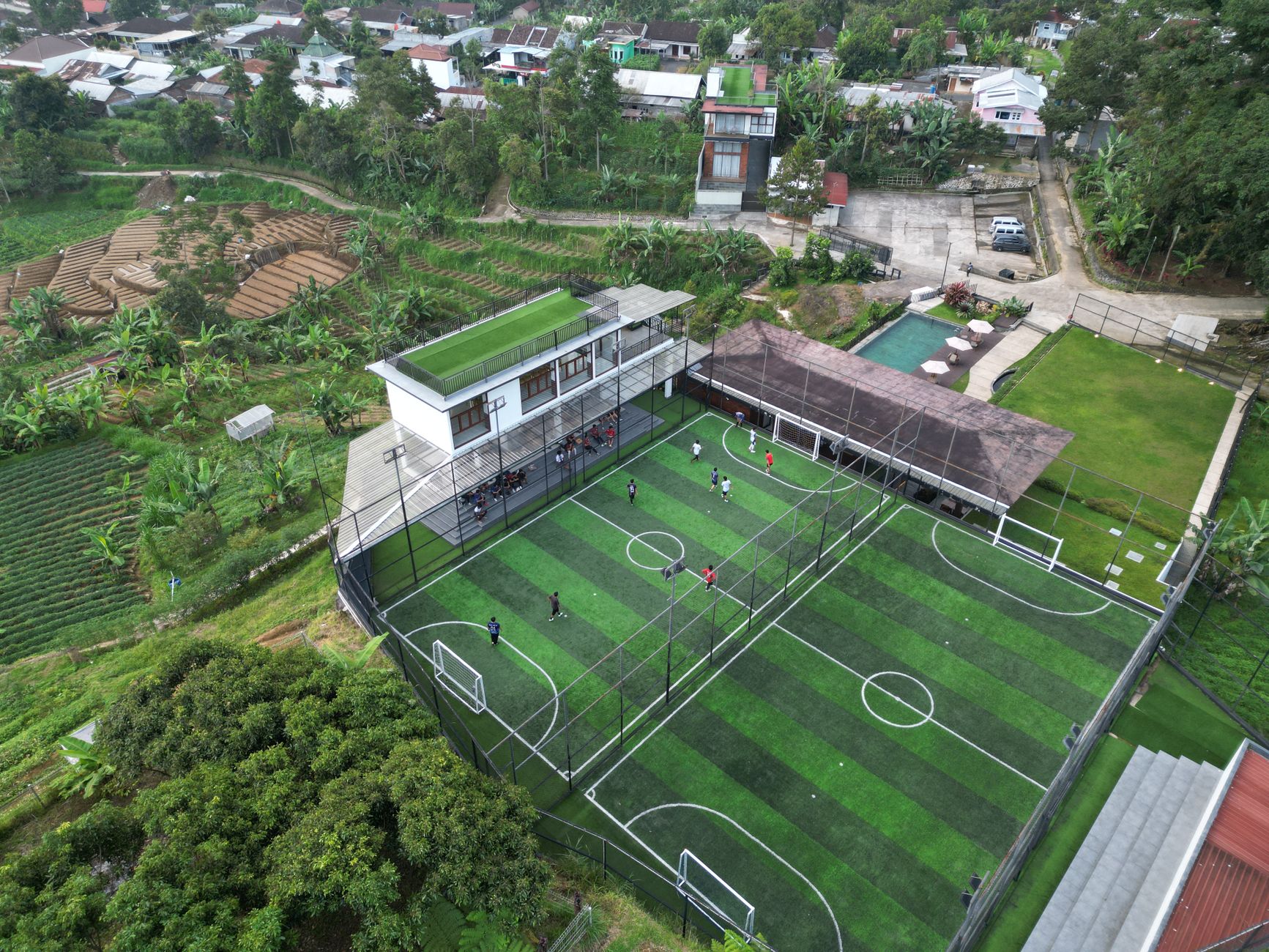 Pemandangan udara lapangan sepak bola yang semarak di Jawa Tengah, Indonesia, dikelilingi oleh pepohonan hijau yang rimbun.