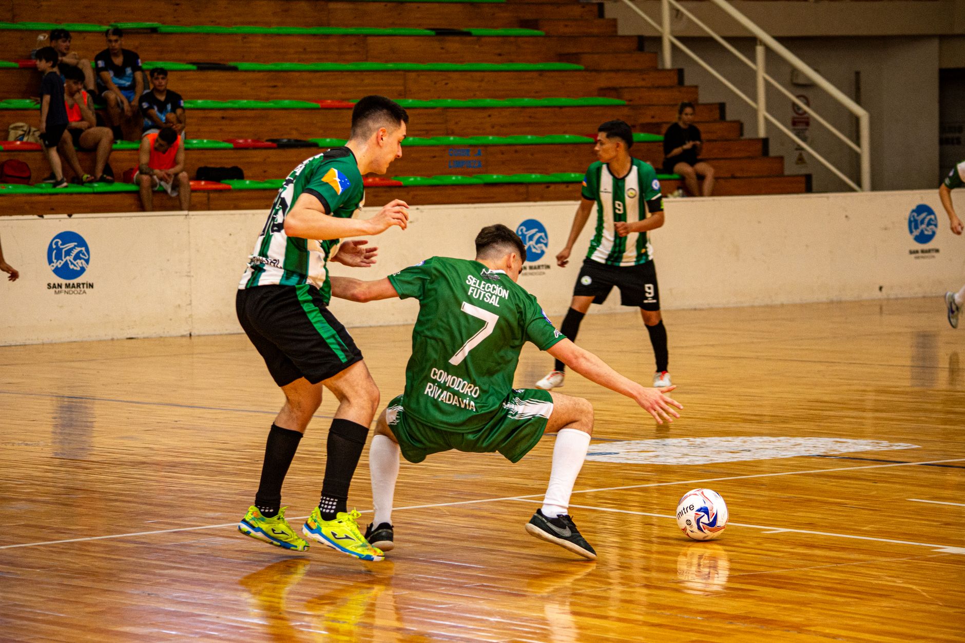 Pertandingan futsal dalam ruangan yang mendebarkan dengan atlet yang bersaing di lapangan kayu yang dipoles.