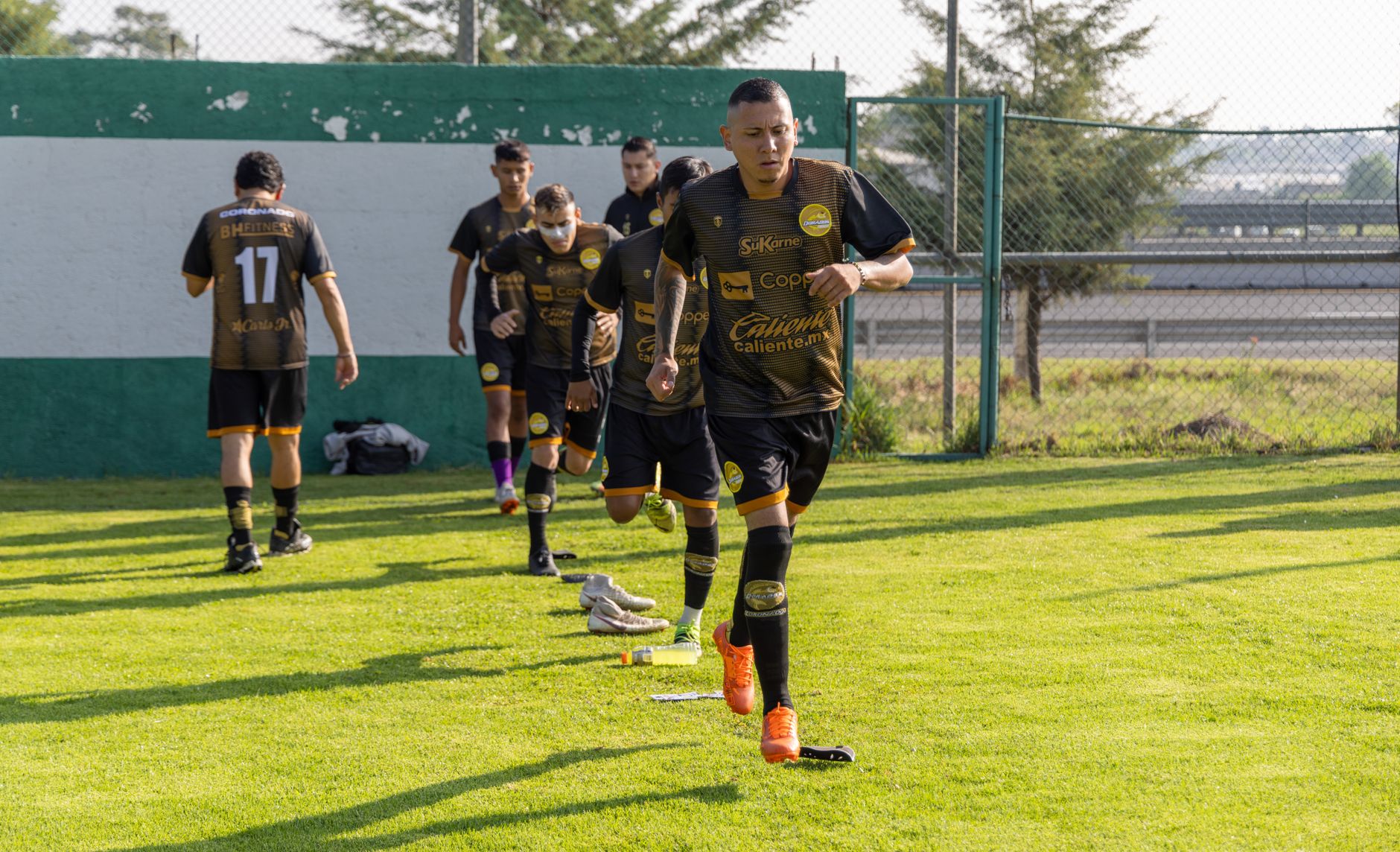 Tim sepak bola melakukan pemanasan di lapangan, mengenakan seragam olahraga.
