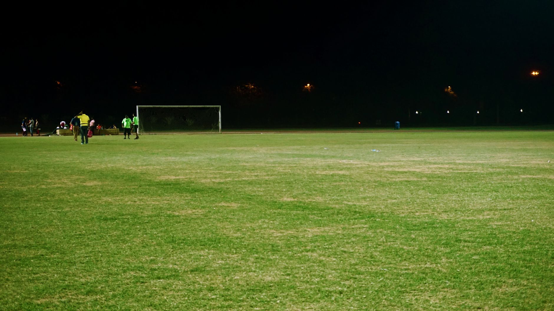 Pemandangan lapangan sepak bola di malam hari dengan pemain dan tiang gawang di bawah lampu sorot.