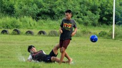Dua remaja terlibat dalam pertandingan sepak bola yang seru di lapangan berumput, menampilkan aksi dan sportivitas.