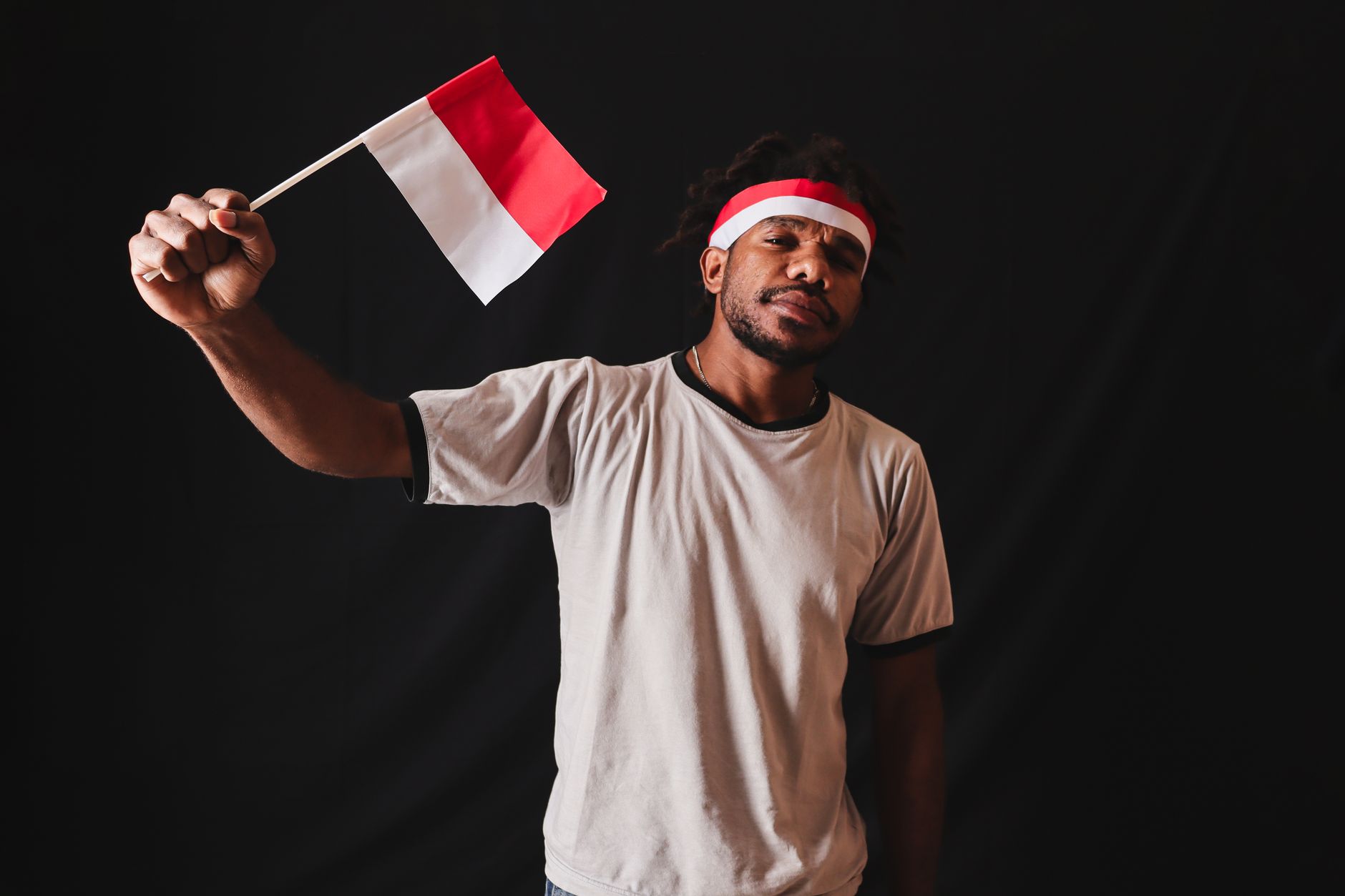 Pria Papua memegang bendera Indonesia, melambangkan patriotisme dan kebanggaan budaya dalam suasana studio.