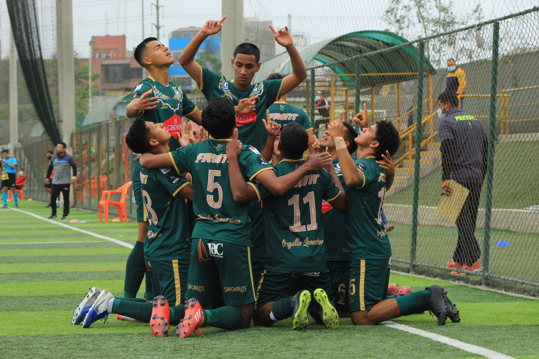 Anggota tim sepak bola remaja merayakan gol di lapangan, menunjukkan kerja sama tim dan semangat.