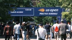 Orang-orang berkumpul di papan jadwal latihan US Open di bawah langit yang cerah.